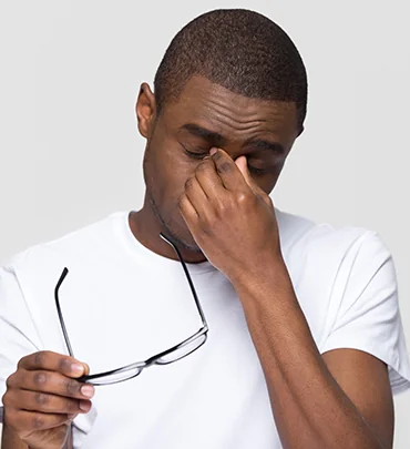 Person holding eyeglasses and rubbing one eye